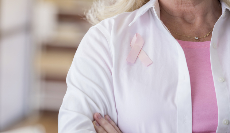 A woman in a white coat wearing a breast cancer awareness ribbon.