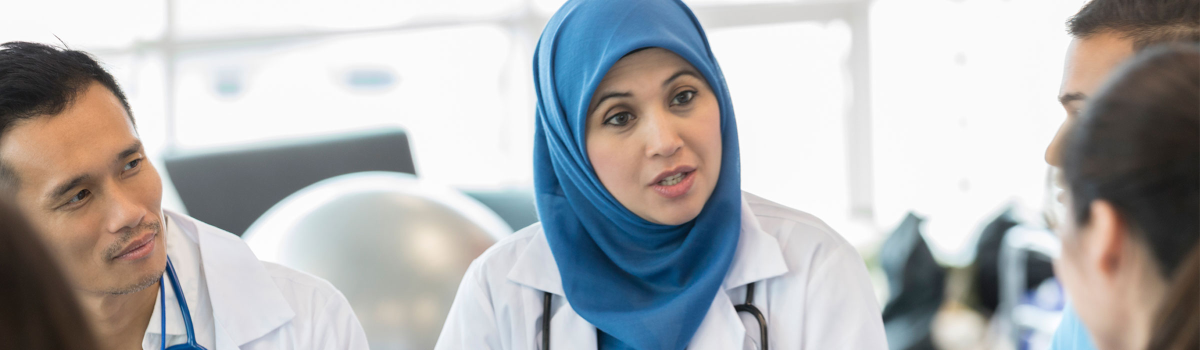Female doctor wearing a hijab talking to other doctors. 