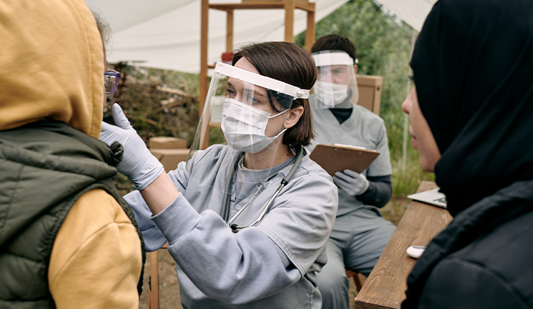 Female doctor wearing surgical mask and shield evaluates a patient