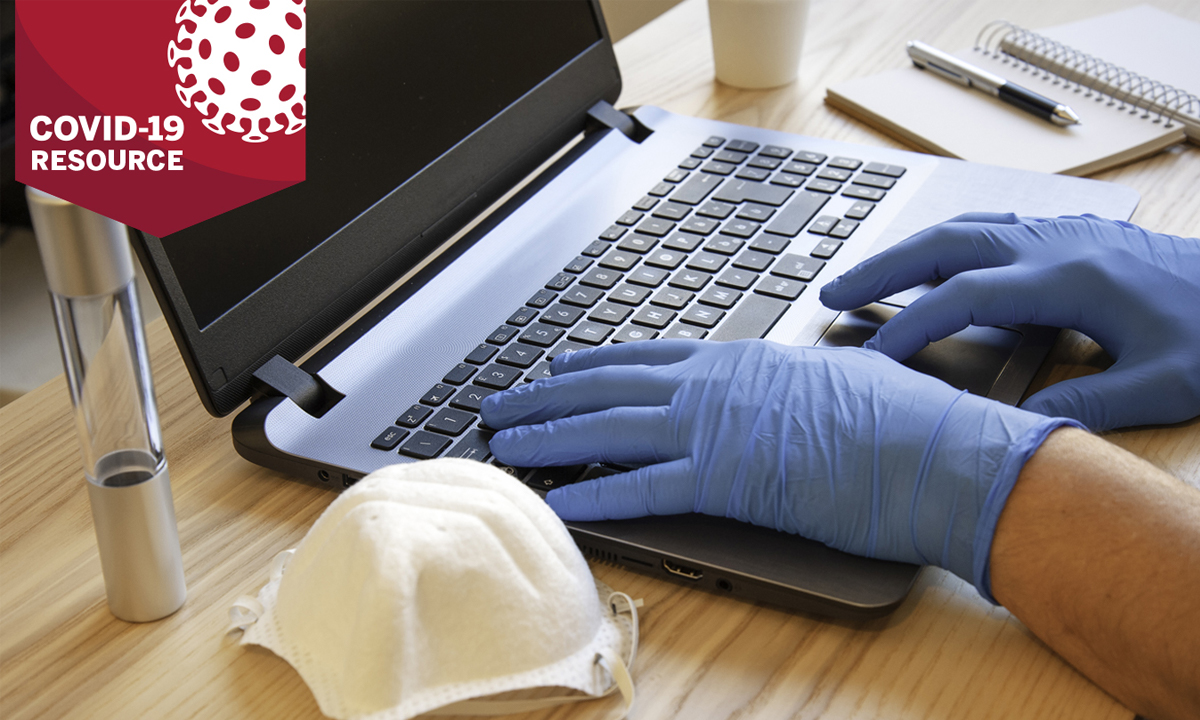 Clinician typing on a computer with gloves and a mask next to it