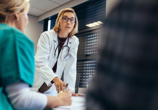 A female surgeon pointing to a document on a table.