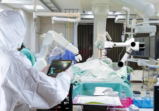 A surgeon in PPE utilizing a robot to preform surgery.