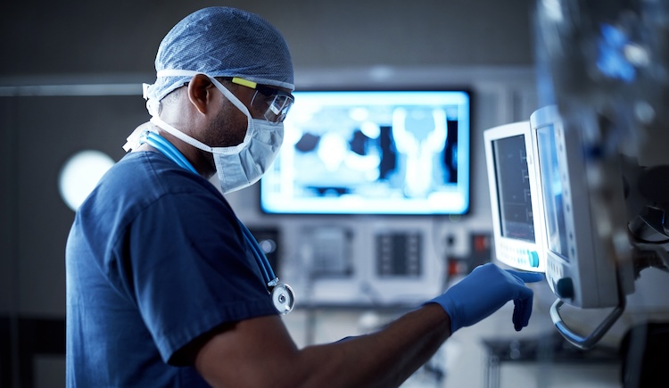 A health care provider dressed in surgical personal protective equipment looks at a screen in an operating room.