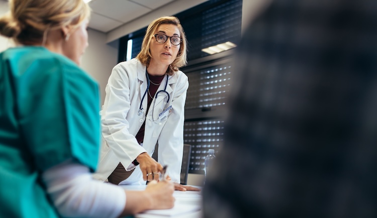 A female surgeon pointing to a document on a table.