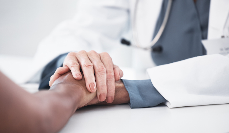 A physician holding the hand of a patient in comfort.