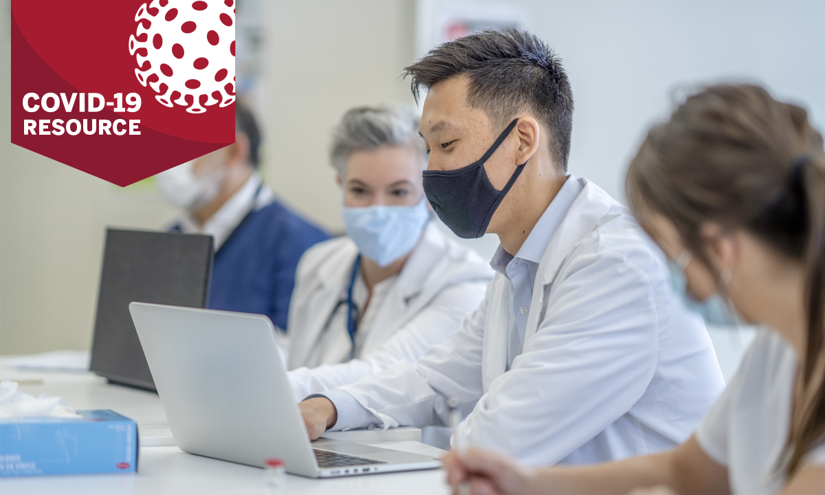 Medical professionals in masks at a desk looking at computer with COVID-19 Resource banner