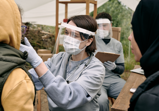 Female doctor wearing surgical mask and shield evaluates a patient