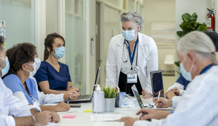 Group of doctors in masks having a conversation around a white table