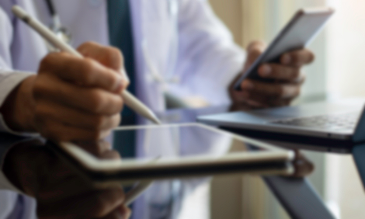 Blurry image of a physician using a stylus with an ipad and holding a phone